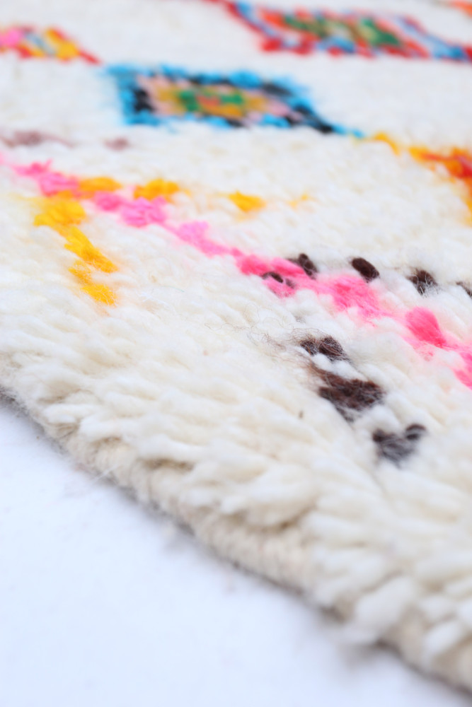 Tapis berbère aux motifs colorés, dominé par des teintes crème, rose, bleu et jaune sur fond clair.