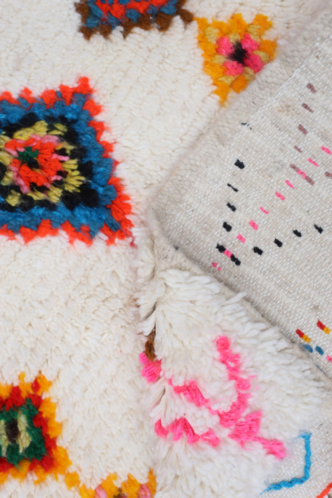 Tapis berbère coloré avec motifs géométriques aux teintes vives de rouge, bleu, jaune et rose sur fond crème.