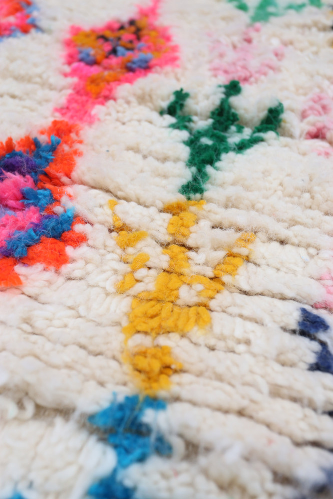 Tapis berbère au design coloré, avec des nuances de blanc, jaune, vert, rose et bleu, ornés de motifs géométriques.