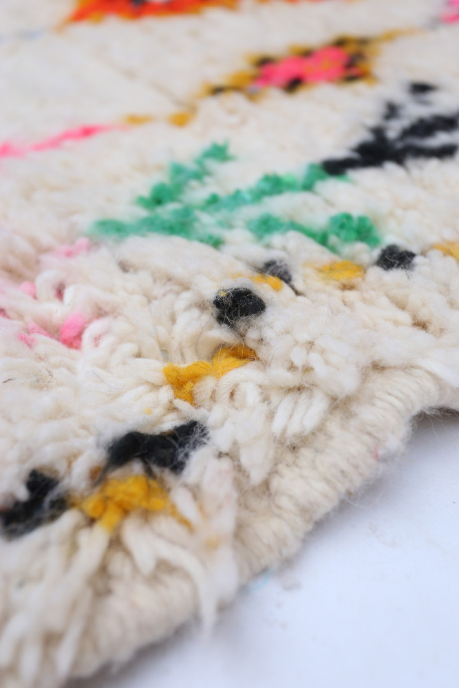 Tapis berbère aux motifs colorés de rose, noir, jaune et vert sur fond crème.