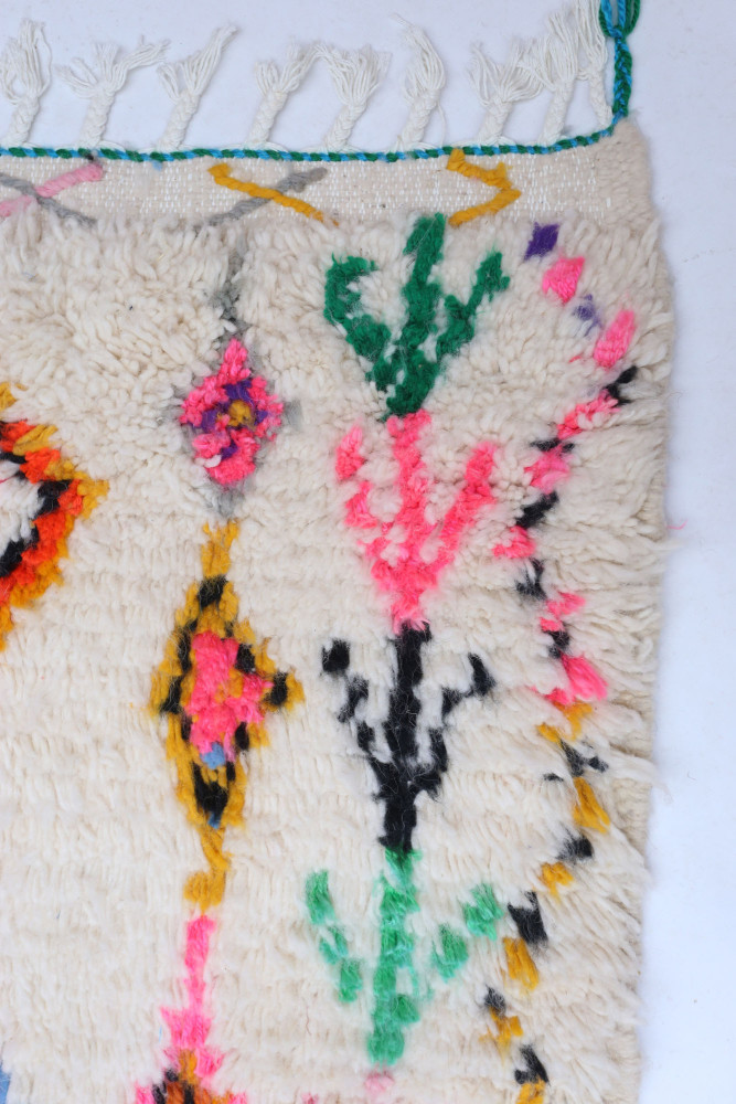 Tapis berbère aux motifs floraux colorés, dominé par des teintes blanches, roses, vertes et noires.
