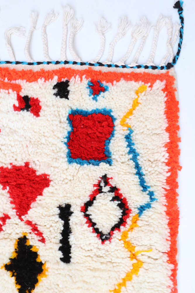 Tapis berbère coloré avec des motifs géométriques rouges, bleus et noirs sur fond crème, idéal pour un intérieur moderne.