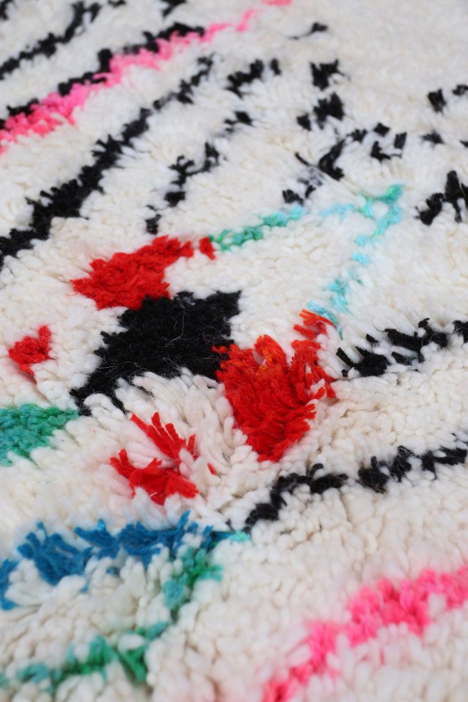 Tapis berbère en laine au fond crème, décoré de motifs géométriques en noir, rouge, bleu et rose éclatant.