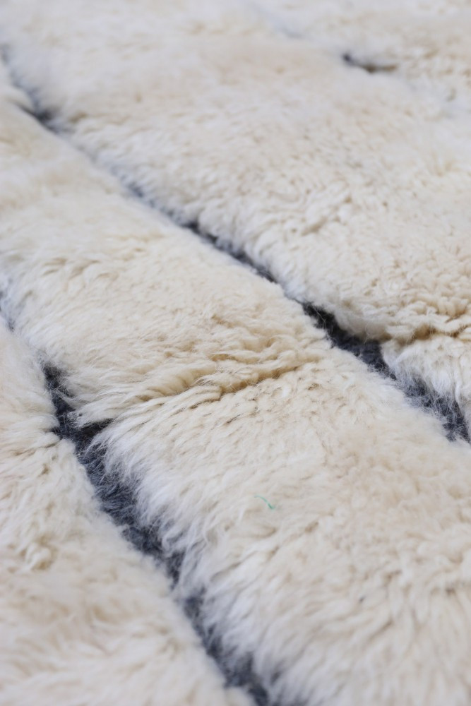 Tapis berbère en laine crème avec des motifs géométriques noirs, offrant chaleur et élégance pour un intérieur moderne.
