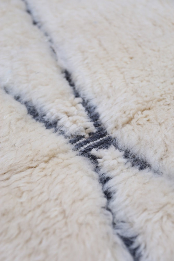 Tapis berbère aux teintes crème et noir, avec des motifs de lignes géométriques délicates et texture moelleuse.