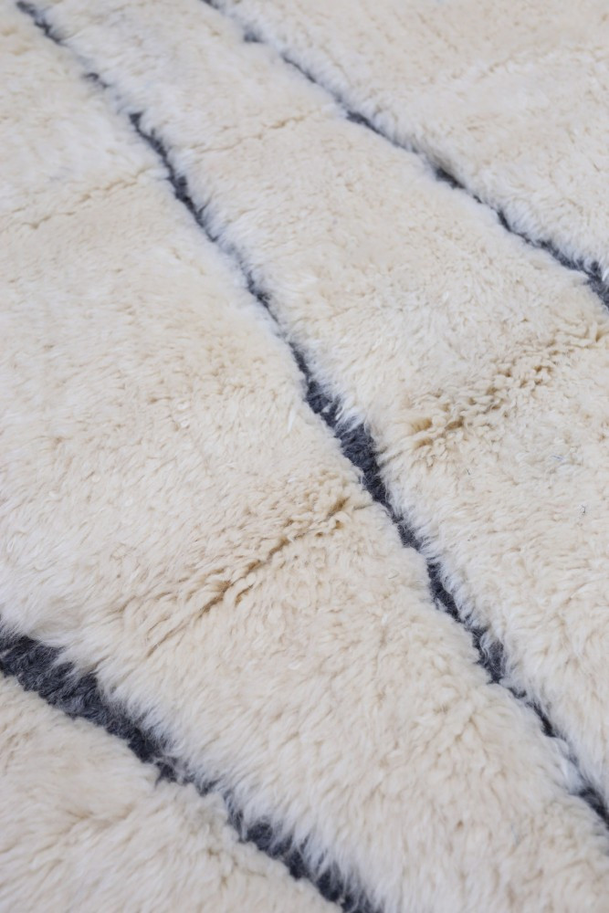 Tapis berbère en laine écrue avec des motifs géométriques noirs et des lignes délicates, apportant élégance et confort.