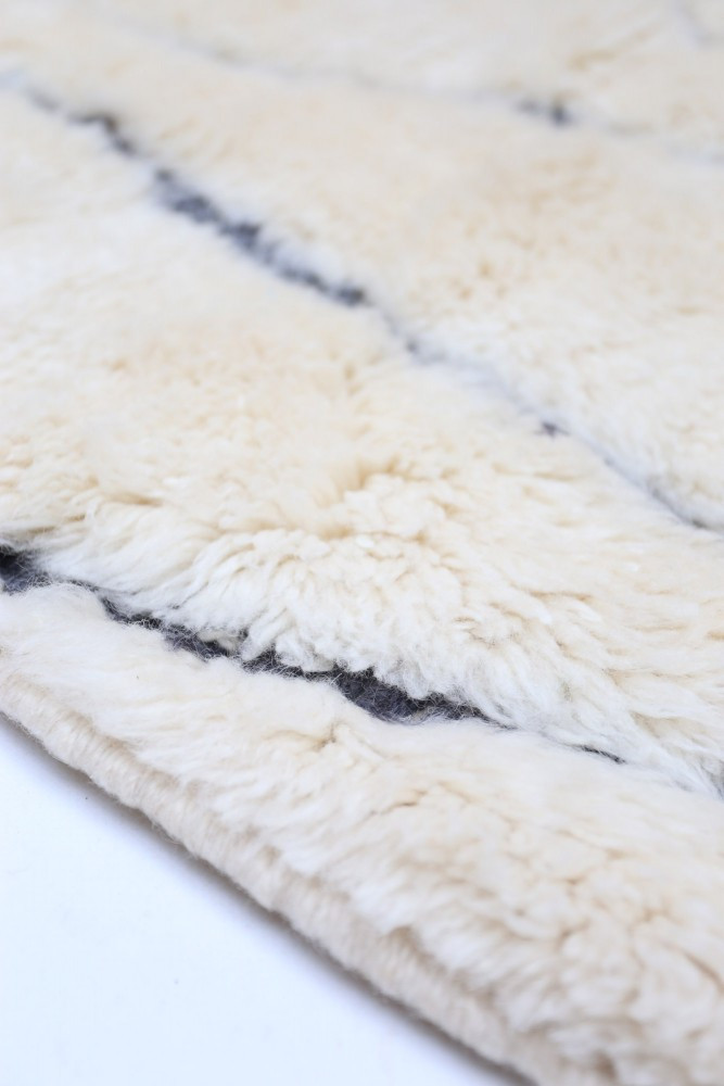 Tapis berbère en laine au style minimaliste, aux nuances crème et motifs géométriques noirs.