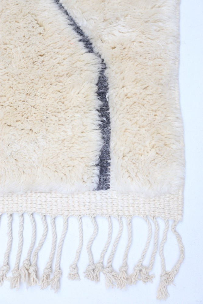 Tapis berbère en laine crème avec motifs géométriques noirs et franges délicates pour une touche chaleureuse et authentique.