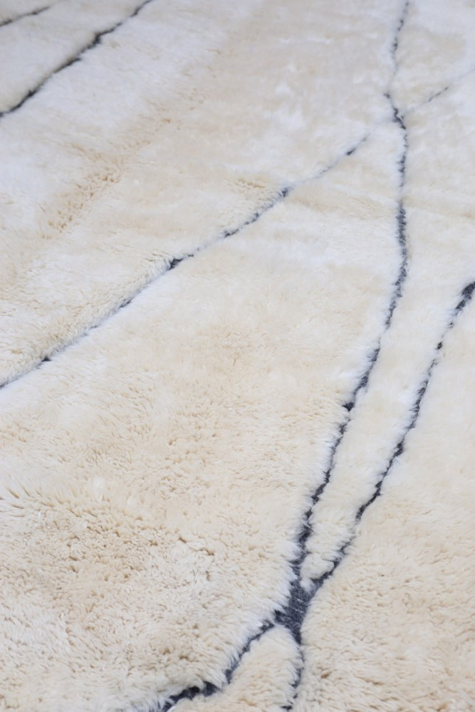 Tapis berbère en laine beige avec des motifs géométriques noirs, offrant une texture douce et moderne.