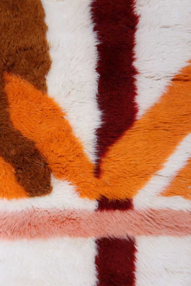 Tapis berbère aux teintes chaudes de orange, marron et rouge, avec des motifs géométriques sur fond crème.