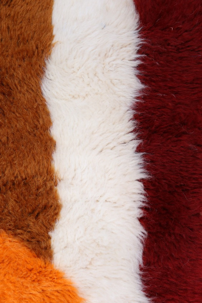 Tapis berbère en laine, aux couleurs chaudes d\'orange, brun, rouge et blanc, avec des motifs doux et texturés.