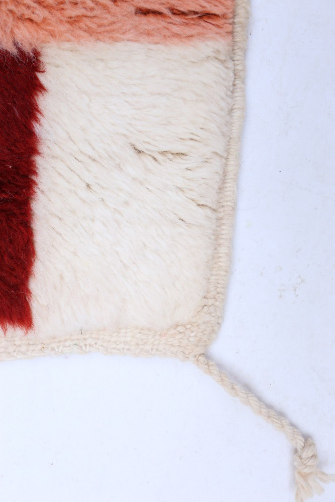 Tapis berbère aux motifs géométriques en rouge, crème et orange, offrant une texture douce et chaleureuse.