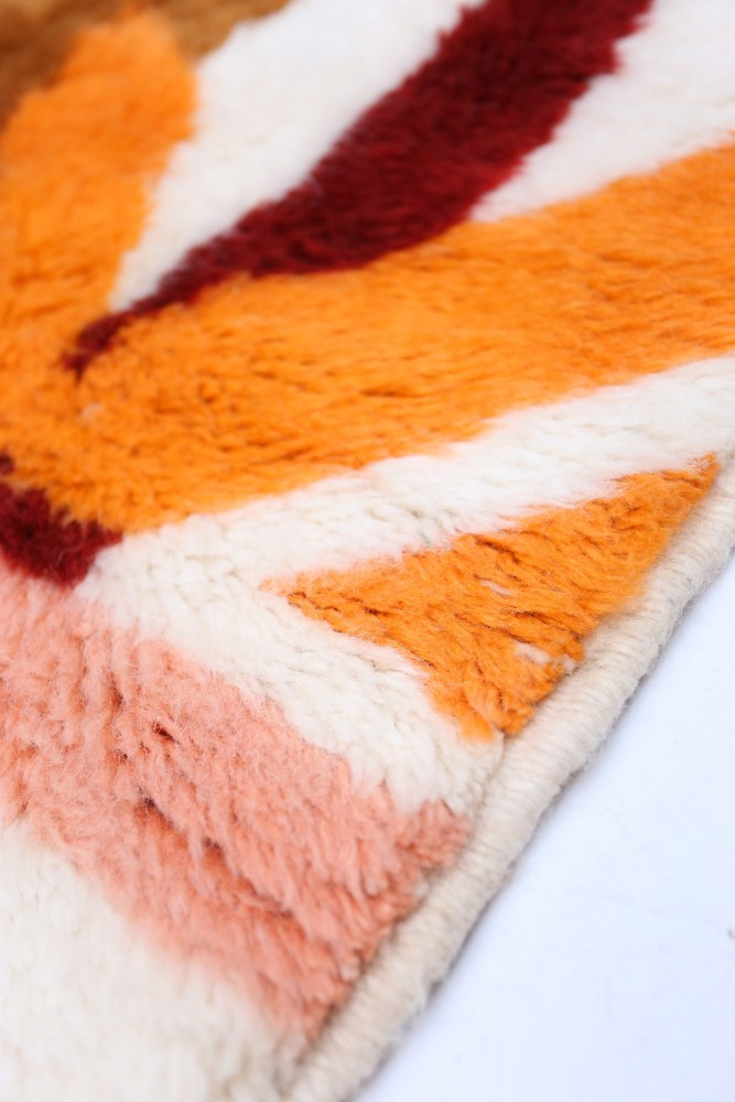 Tapis berbère aux motifs géométriques colorés, dominé par l\'orange, le rouge et le rose, pour une ambiance chaleureuse.