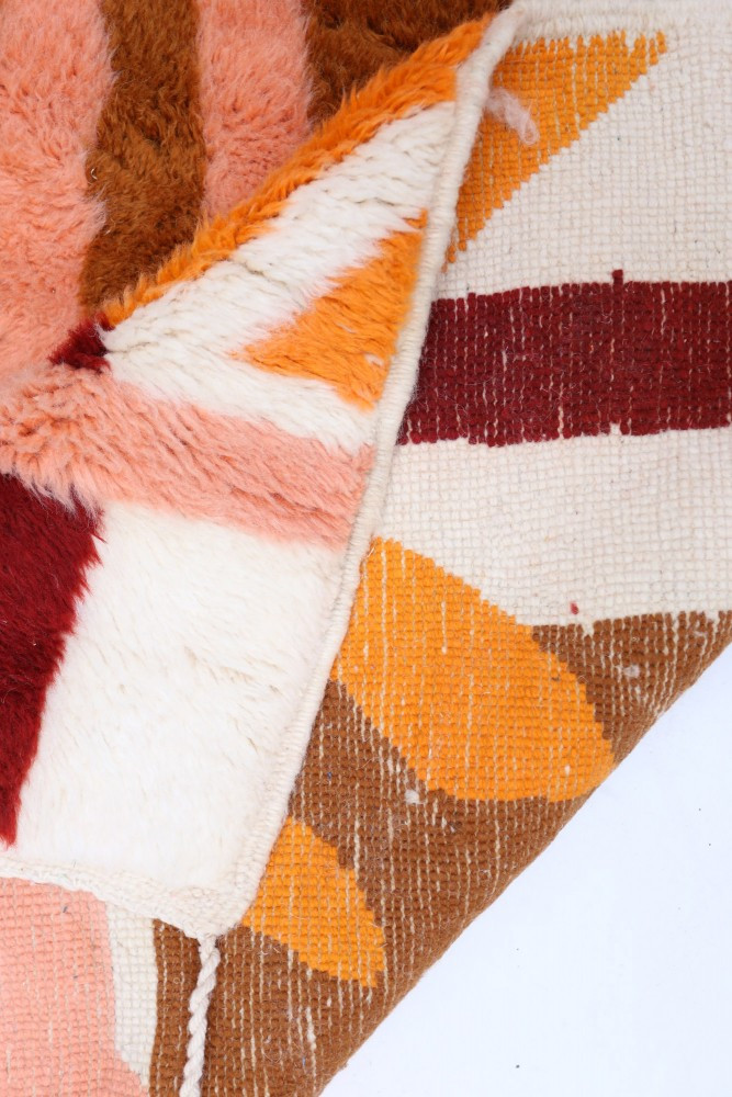 Tapis berbère aux motifs géométriques, couleurs chaudes d\'orange, rouge et marron sur fond crème.