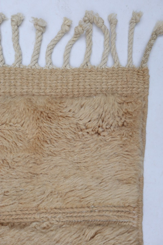 Tapis berbère en laine beige, au style ethnique, avec des motifs tissés et des franges délicates.