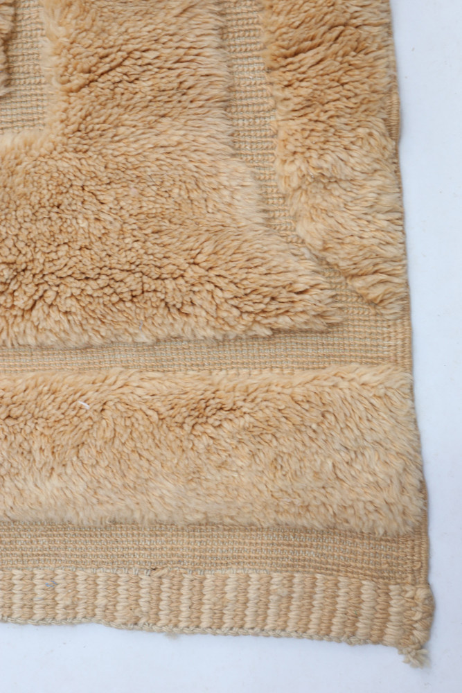 Tapis berbère en laine beige avec des motifs texturés et des rayures subtiles pour une ambiance chaleureuse et élégante.