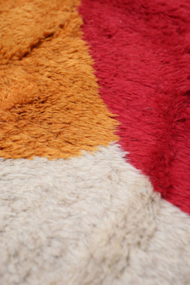 Tapis berbère aux motifs géométriques, dans des tons rouge, orange et beige, offrant une texture douce et chaleureuse.
