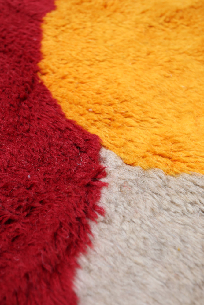 Tapis berbère aux teintes vives de rouge, orange et beige avec des motifs organiques et une texture douce et laineuse.