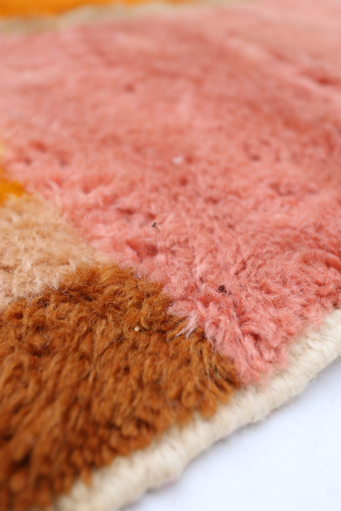 Tapis berbère aux couleurs vives, mélange de rose, orange et marron avec des motifs géométriques uniques.