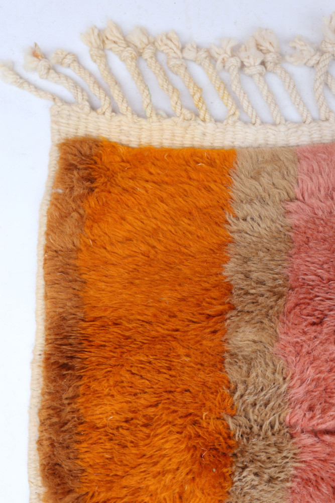 Tapis berbère aux teintes orange, beige et rose avec des motifs doux et des franges élégantes.