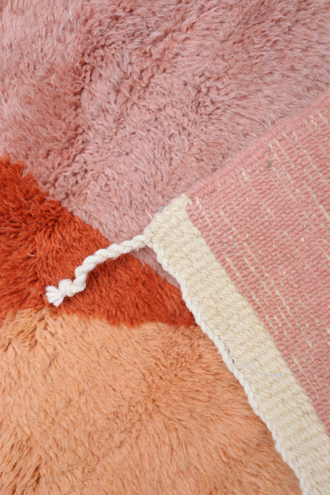 Tapis berbère aux couleurs pastel de rose et orange, avec des motifs texturés et un aspect doux et chaleureux.