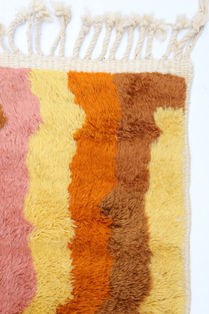 Tapis berbère aux motifs géométriques, avec des couleurs vives comme le rose, orange, et jaune sur un fond doux.