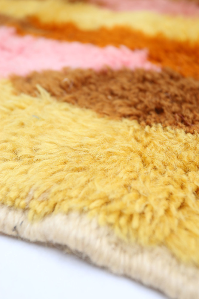 Tapis berbère aux couleurs jaune, orange, rose et marron avec des motifs texturés doux et modernes.
