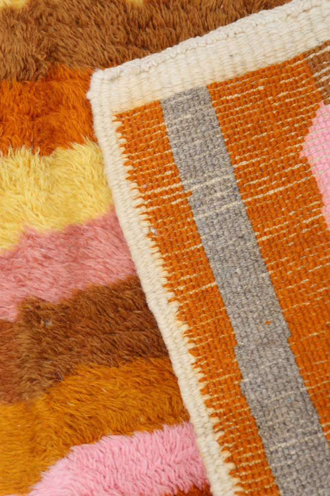Tapis berbère coloré avec des nuances de rose, orange et marron, présentant des motifs géométriques vibrants.
