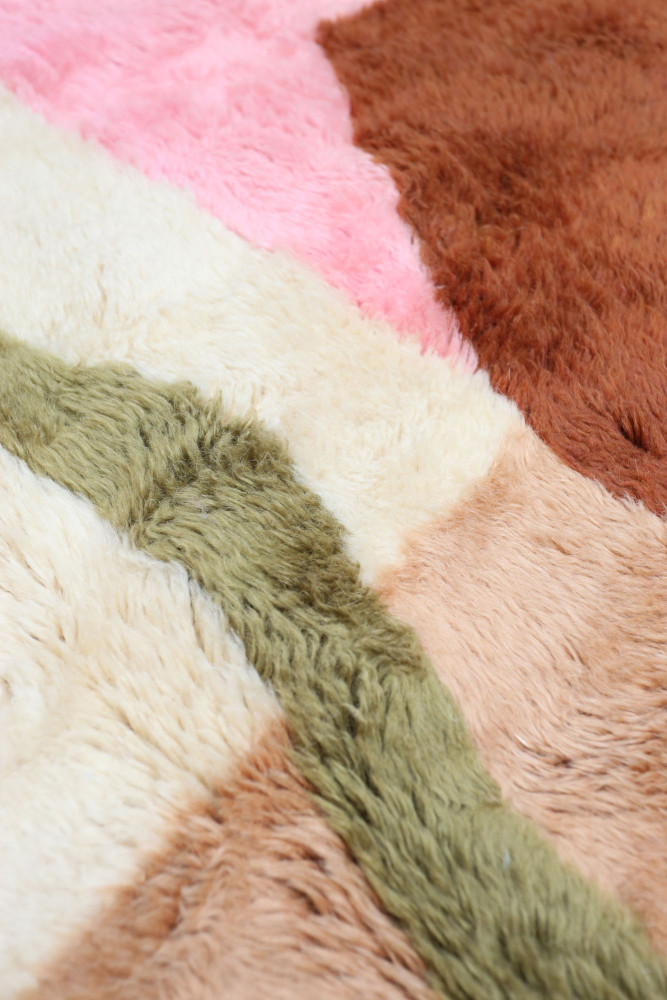 Tapis berbère aux motifs géométriques avec des couleurs pastel comme le rose, le beige, le marron et le vert.