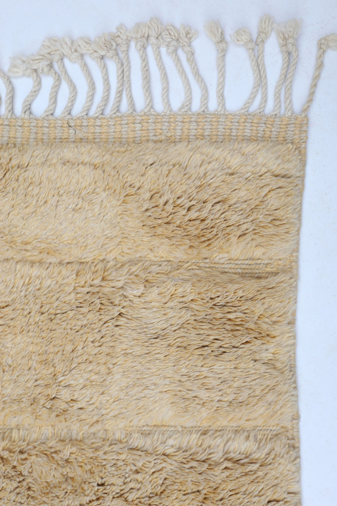 Tapis berbère en laine beige, au style artisanal, avec des motifs texturés et des franges délicates.
