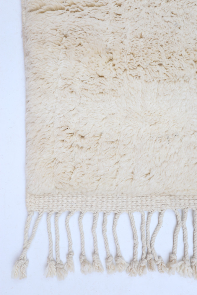 Tapis berbère en laine au style minimaliste, coloris crème avec des motifs texturés et des franges délicates.