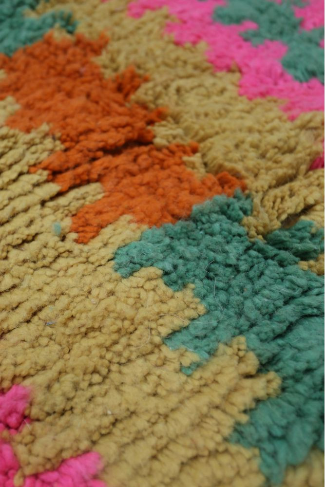 Tapis berbère aux couleurs vives avec des motifs géométriques en rose, orange et vert sur fond beige.