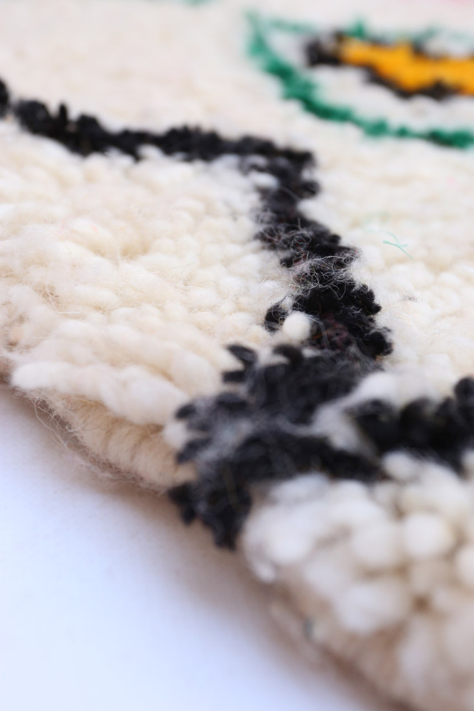 Tapis berbère en laine blanche avec des motifs géométriques noirs et verts, ajoutant une touche artisanale et élégante.
