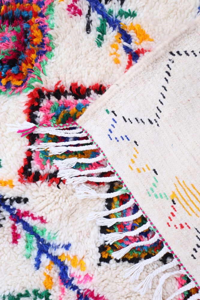 Tapis berbère coloré avec des motifs floraux vibrants sur fond crème et des franges délicates.