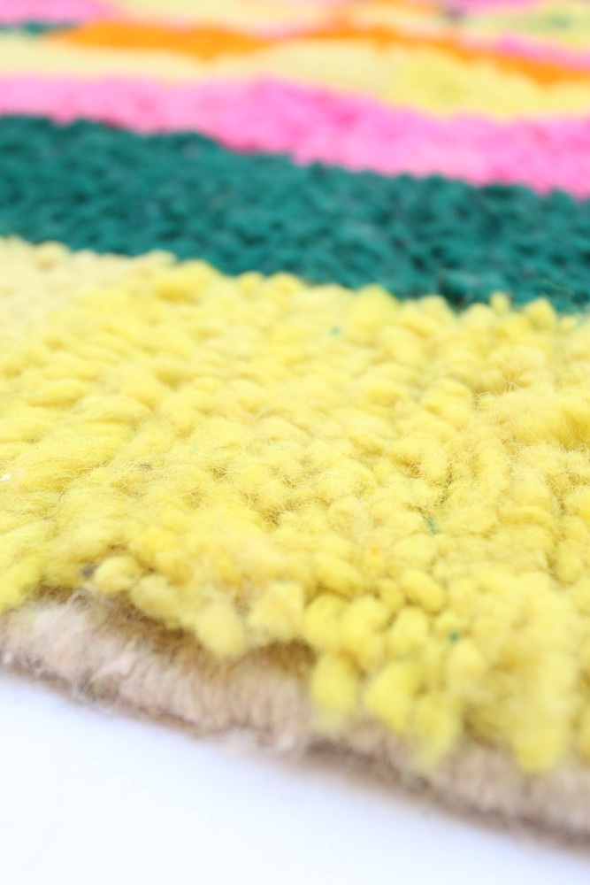 Tapis berbère aux couleurs vives avec des motifs géométriques, incluant du jaune, du rose, du vert et du beige.