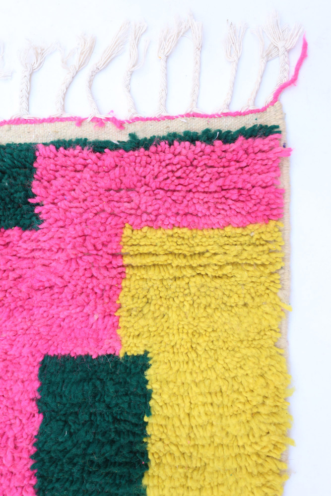 Tapis berbère coloré avec des motifs géométriques en rose, jaune et vert, parfaitement texturé et moderne.