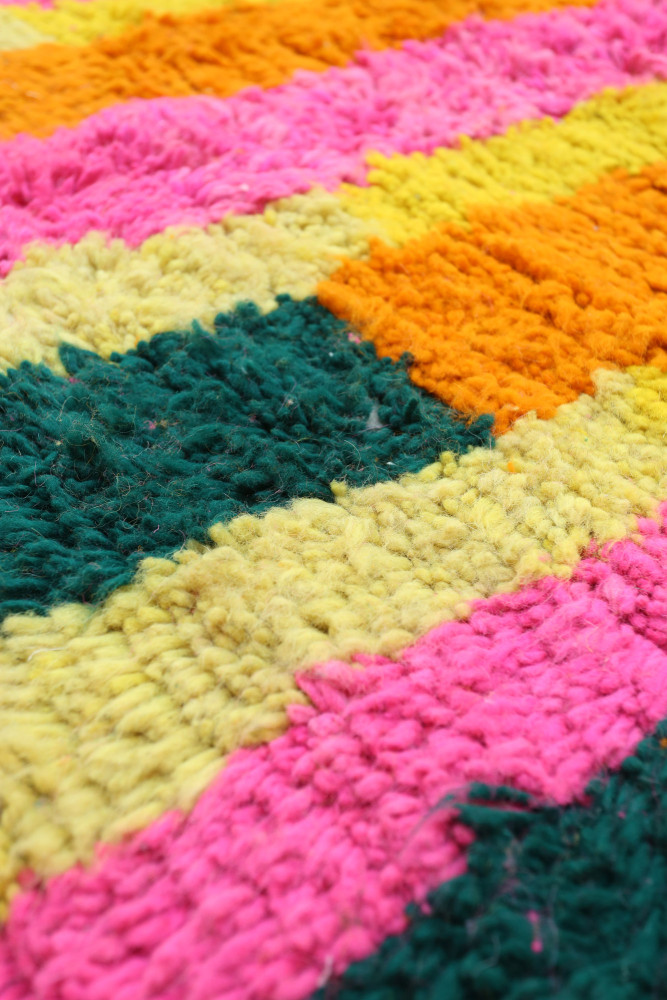 Tapis berbère coloré avec des motifs géométriques en rose, orange, jaune et vert, apportant une touche moderne et vibrante.