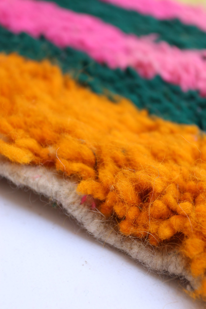 Tapis berbère coloré avec des motifs en zigzag violet, orange et vert, idéal pour une décoration moderne et chaleureuse.