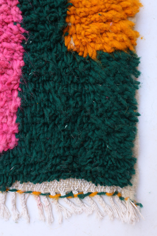 Tapis berbère aux couleurs vives de vert, orange et rose, avec des motifs texturés et une finition soignée.