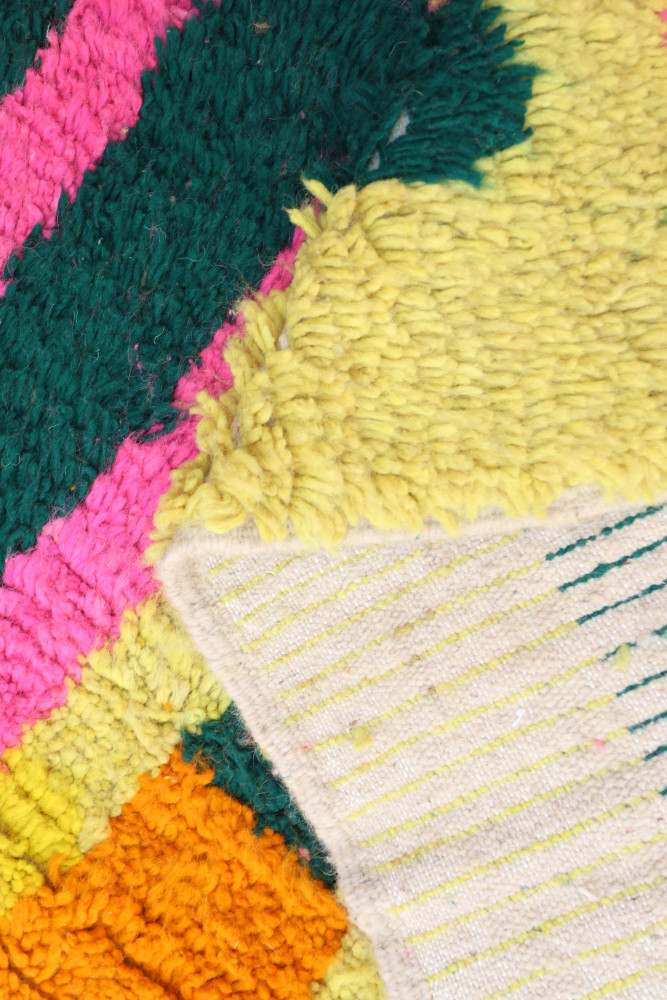 Tapis berbère coloré avec des motifs géométriques en jaune, vert, rose et orange sur un fond clair.