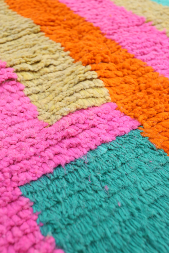 Tapis berbère coloré avec des rayures vives en rose, orange, vert et beige, au style moderne et texturé.