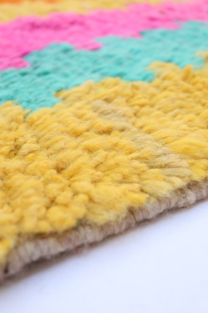 Tapis berbère coloré avec des motifs géométriques en jaune, rose et vert, ajoutant une touche moderne à votre intérieur.
