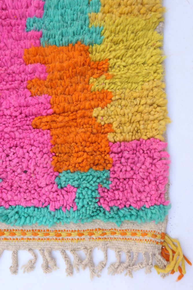 Tapis berbère coloré à motifs géométriques en rose, orange, jaune et vert, parfait pour une décoration moderne et chaleureuse.