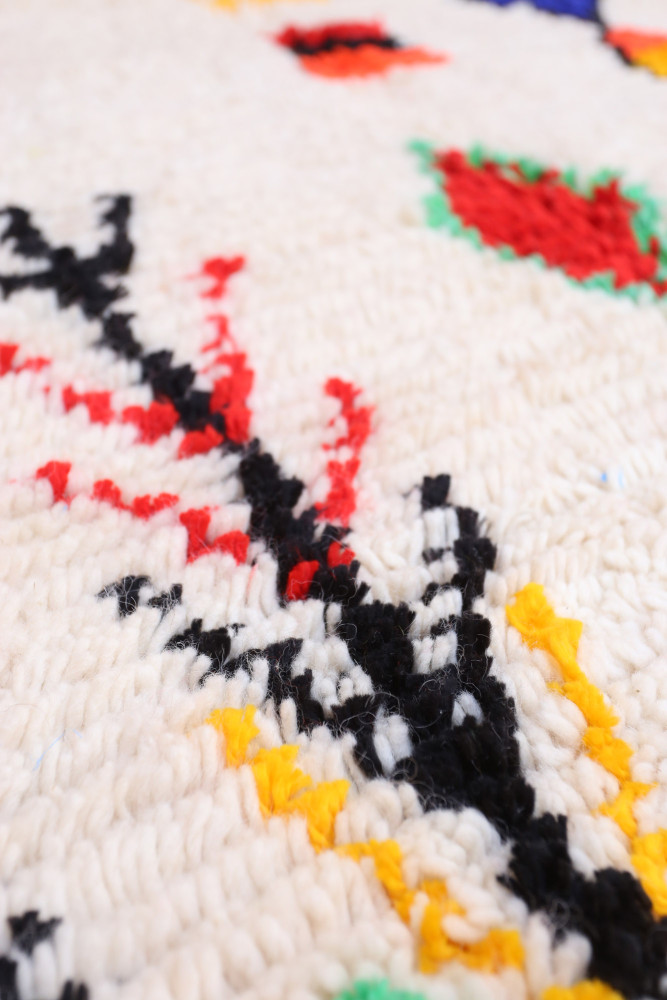 Tapis berbère aux motifs colorés, dominé par le blanc, le rouge, le noir et le jaune, offrant un style artisanal et chaleureux.