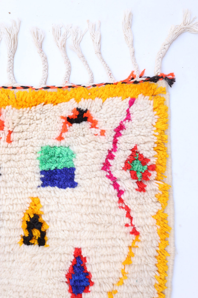 Tapis berbère aux motifs colorés, dominé par des teintes crème, orange, vert et rouge, avec des formes géométriques.