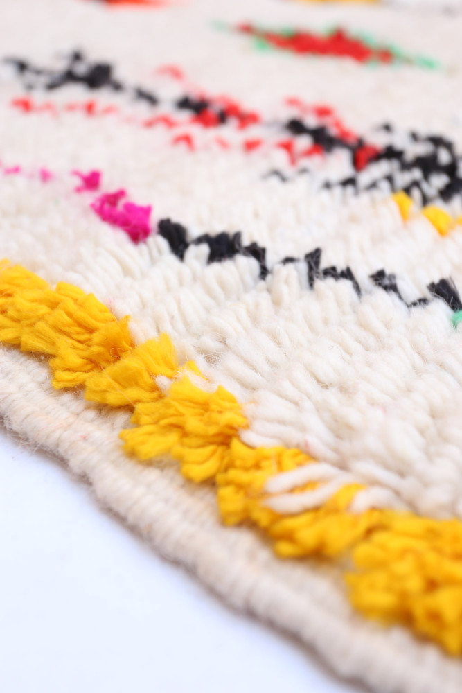 Tapis berbère aux teintes naturelles, motifs colorés en noir, rouge, rose et jaune sur fond crème.