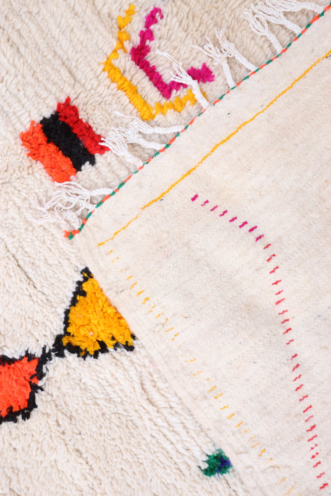 Tapis berbère aux couleurs vives, avec des motifs géométriques et des franges, idéal pour un décor chaleureux et authentique.