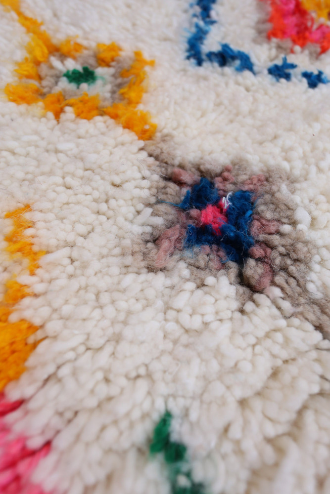 Tapis berbère aux motifs colorés, dominé par le blanc, le jaune et des touches de couleur rouge et bleu.