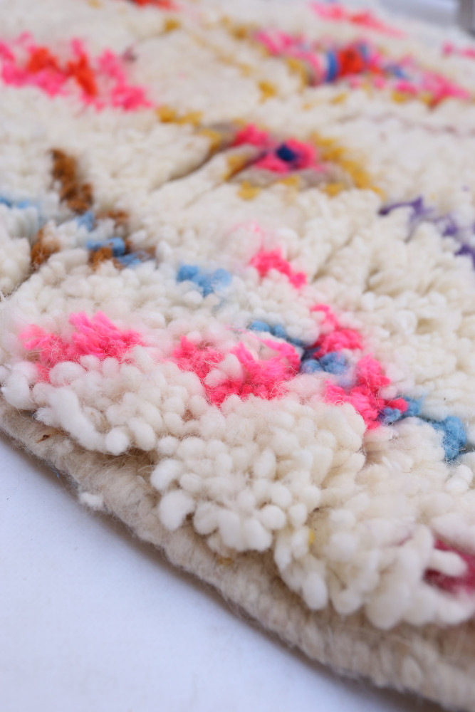 Tapis berbère aux couleurs vives avec des motifs géométriques sur un fond crème.