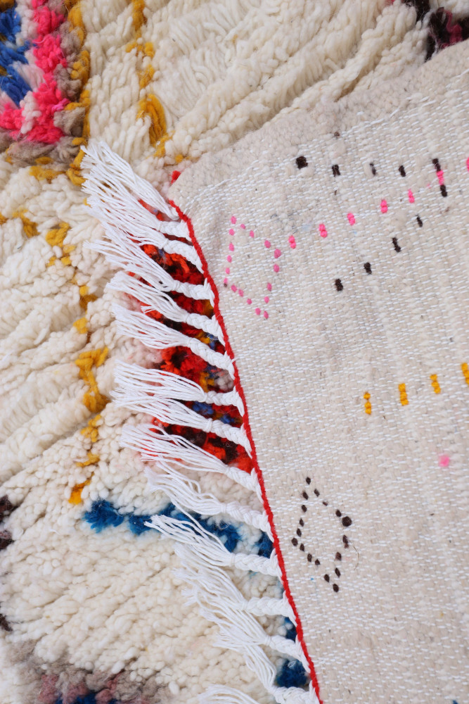Tapis berbère en laine avec motifs colorés rouge, bleu et jaune sur fond crème, ajoutant charme et authenticité à votre espace.